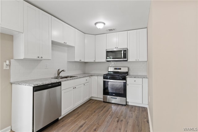 kitchen featuring light stone countertops, white cabinetry, sink, stainless steel appliances, and hardwood / wood-style flooring