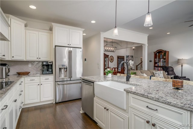 kitchen with stainless steel appliances, a sink, open floor plan, backsplash, and dark wood finished floors