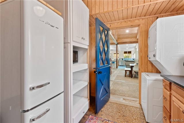 clothes washing area with cabinets, stacked washer and dryer, wooden walls, and wood ceiling