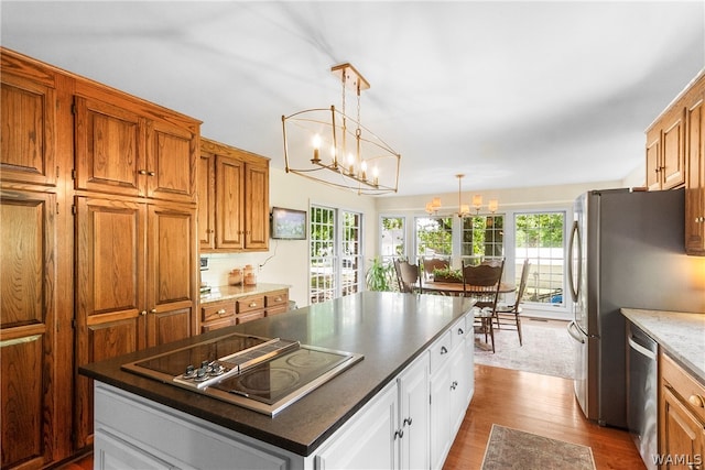 kitchen featuring pendant lighting, an inviting chandelier, light wood-type flooring, appliances with stainless steel finishes, and a kitchen island