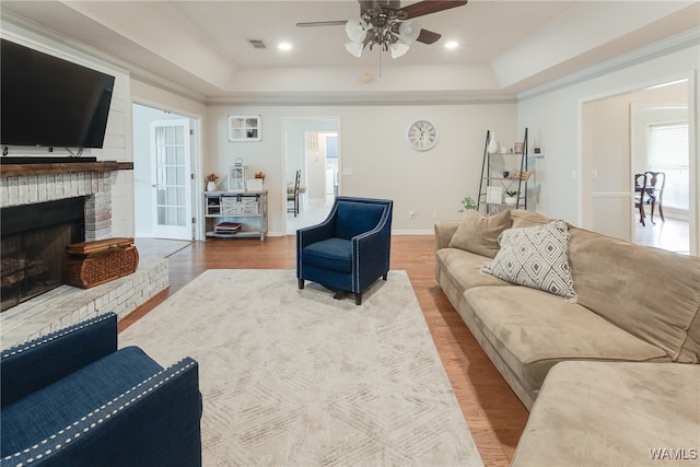 living room featuring ornamental molding, a tray ceiling, hardwood / wood-style flooring, ceiling fan, and a fireplace