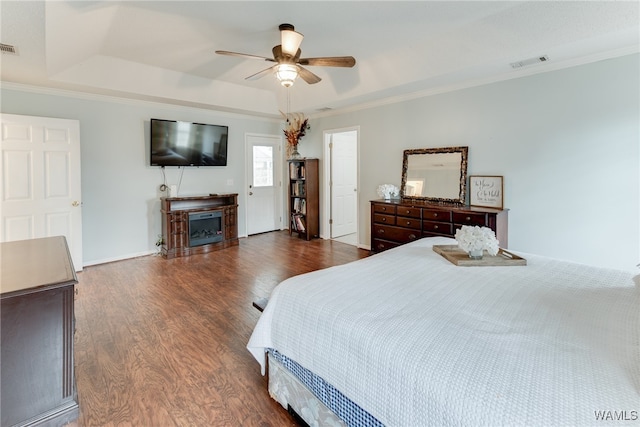 bedroom with ornamental molding, dark wood-type flooring, ceiling fan, and a tray ceiling