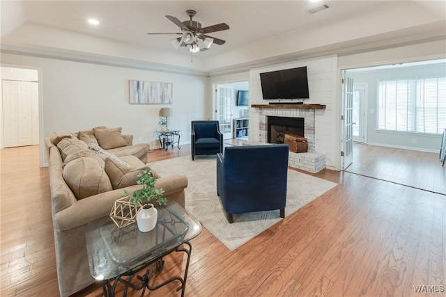 living room featuring a fireplace, light hardwood / wood-style flooring, a raised ceiling, and ceiling fan