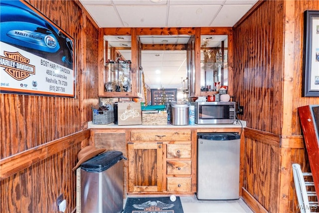 kitchen with a paneled ceiling, wooden walls, and stainless steel appliances