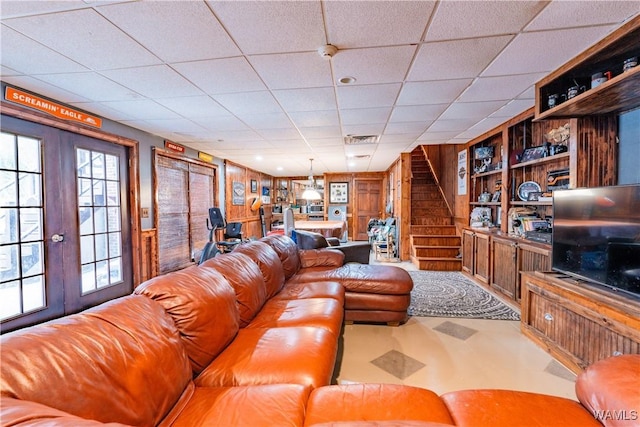 living room with a drop ceiling, built in features, wood walls, and french doors