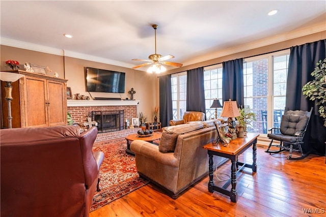 living room featuring light hardwood / wood-style floors, ornamental molding, a brick fireplace, and ceiling fan