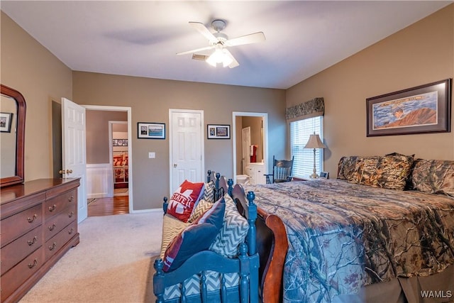 bedroom with ceiling fan, light colored carpet, and connected bathroom