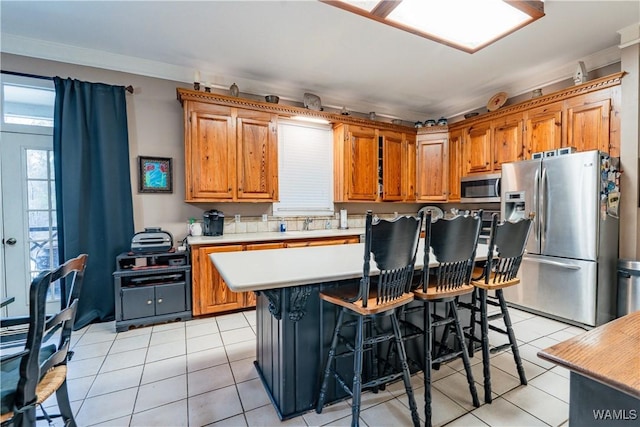 kitchen with light tile patterned floors, a kitchen bar, stainless steel appliances, ornamental molding, and a kitchen island