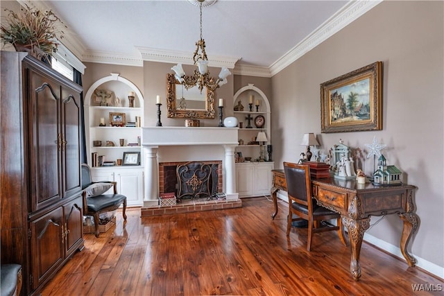 sitting room with built in shelves, dark wood-type flooring, a notable chandelier, and a brick fireplace