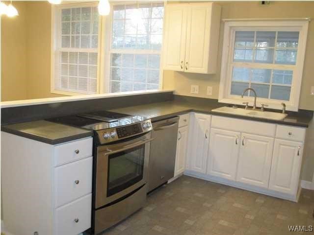 kitchen featuring dark countertops, appliances with stainless steel finishes, white cabinets, and a sink