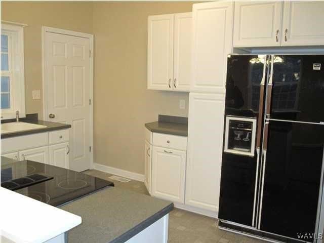 kitchen featuring black appliances, dark countertops, a sink, and white cabinetry