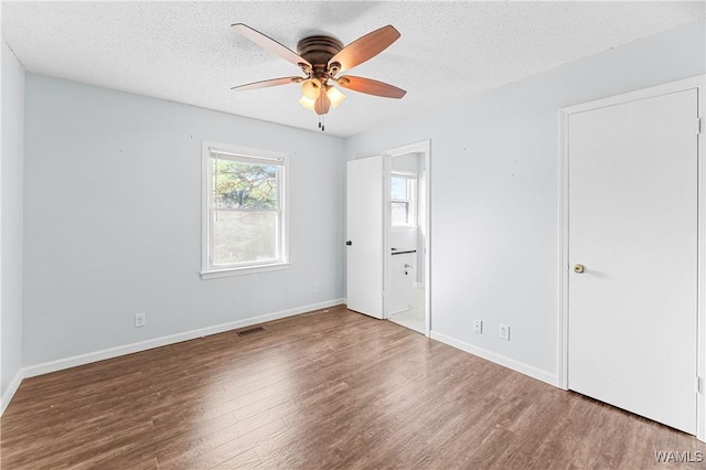 unfurnished bedroom with visible vents, baseboards, wood finished floors, a textured ceiling, and ensuite bath