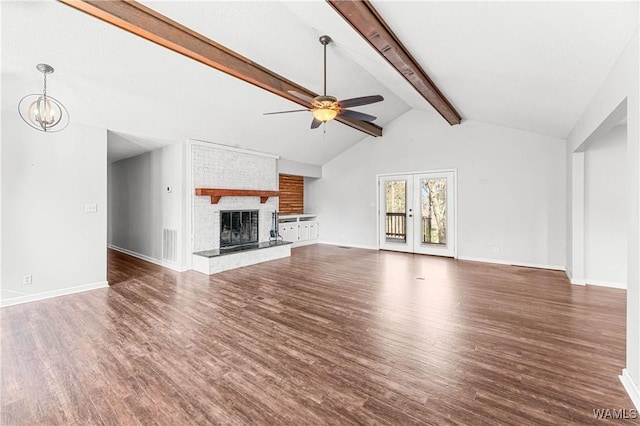 unfurnished living room featuring beam ceiling, ceiling fan with notable chandelier, wood finished floors, baseboards, and a brick fireplace