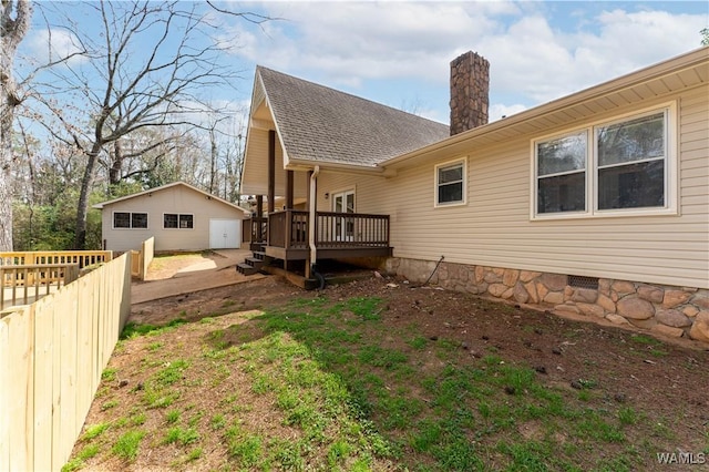 back of house with a shingled roof, fence, a chimney, a deck, and an outbuilding