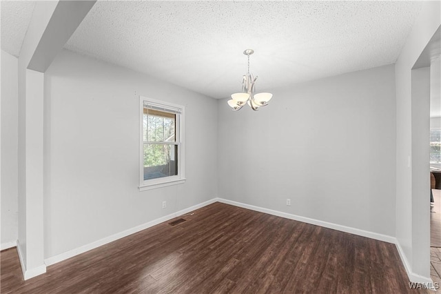 empty room with visible vents, baseboards, dark wood-style floors, and a chandelier