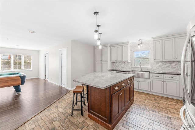 kitchen with a kitchen bar, a sink, backsplash, stainless steel fridge, and baseboards