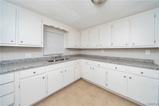 kitchen with a textured ceiling, white cabinets, and sink