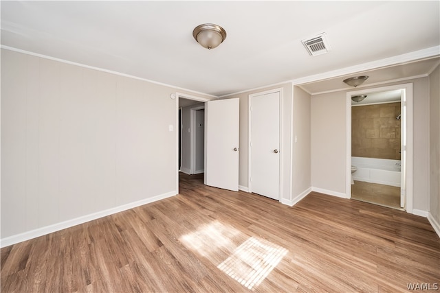 unfurnished bedroom featuring light wood-type flooring, ornamental molding, and ensuite bath