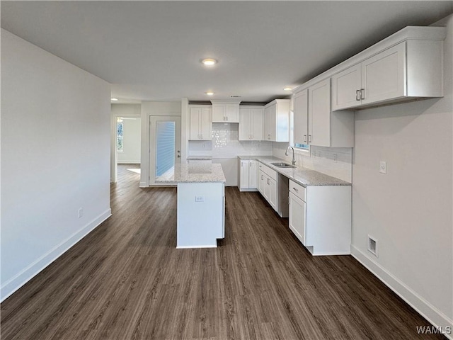 kitchen featuring decorative backsplash, light stone counters, sink, a center island, and white cabinetry