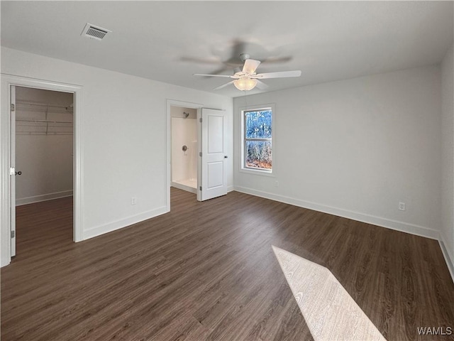 unfurnished bedroom with a closet, a spacious closet, ceiling fan, and dark wood-type flooring