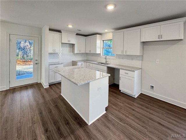 kitchen with light stone counters, a center island, white cabinets, and sink