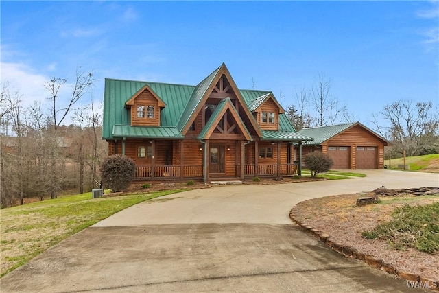 cabin with a porch, a front yard, metal roof, driveway, and a standing seam roof