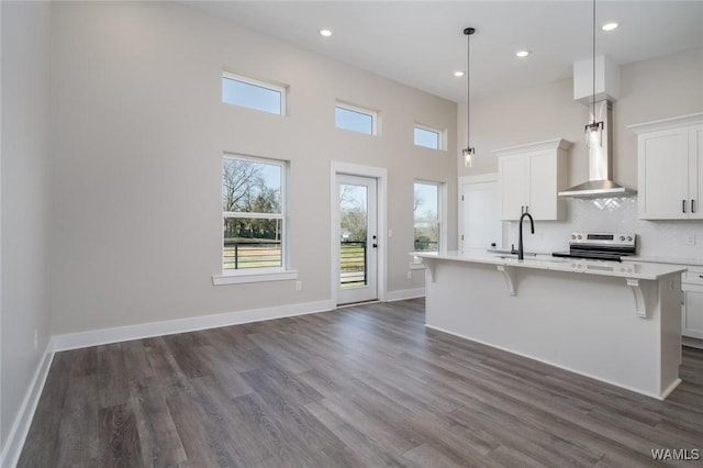 kitchen featuring dark wood-style floors, a center island with sink, light countertops, stainless steel range with electric cooktop, and wall chimney range hood