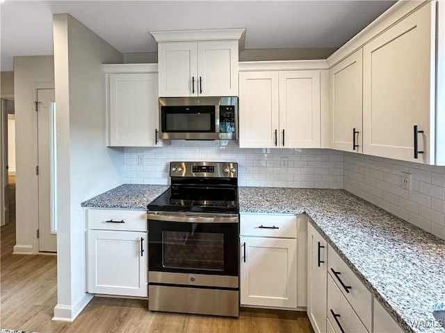 kitchen featuring light stone counters, light wood finished floors, stainless steel appliances, white cabinetry, and tasteful backsplash