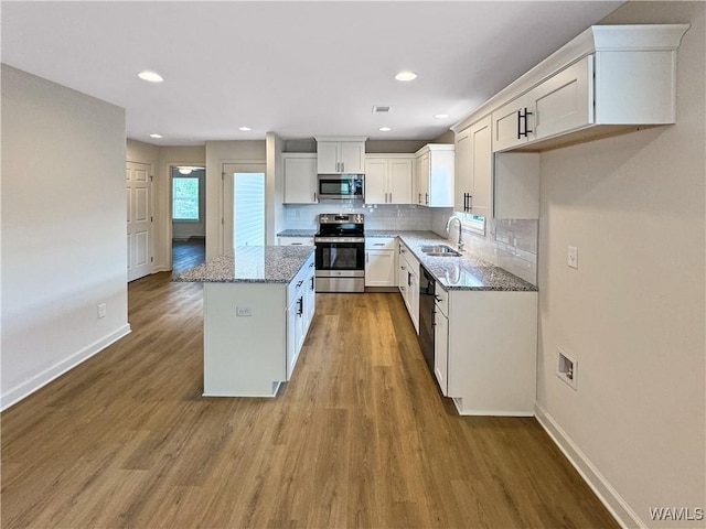 kitchen featuring light stone counters, a center island, stainless steel appliances, white cabinetry, and tasteful backsplash