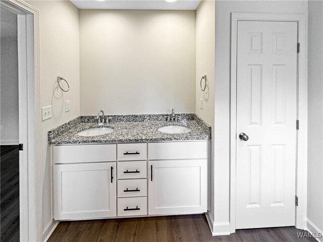 bathroom featuring a sink, baseboards, double vanity, and wood finished floors