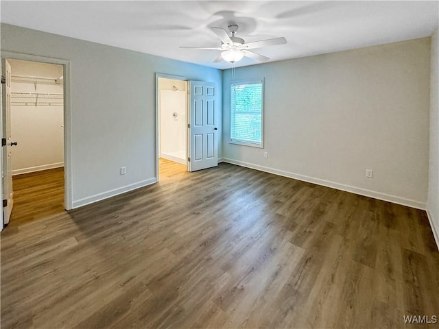 unfurnished bedroom featuring baseboards, dark wood-type flooring, a walk in closet, and a closet