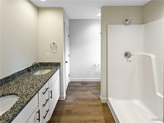 bathroom featuring wood finished floors, double vanity, a sink, and a shower