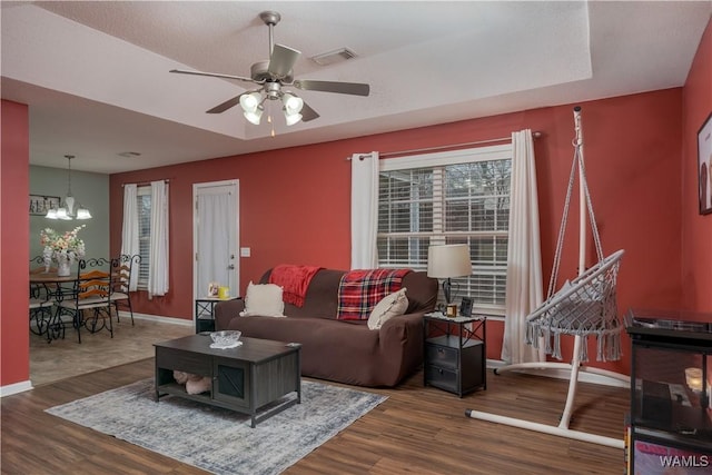 living room featuring a tray ceiling, dark hardwood / wood-style flooring, and ceiling fan with notable chandelier