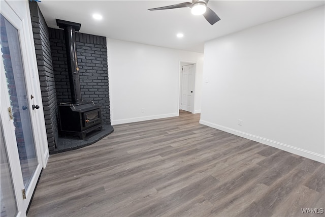 unfurnished living room with a ceiling fan, a wood stove, baseboards, and wood finished floors