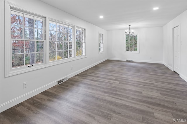 unfurnished dining area featuring an inviting chandelier, plenty of natural light, and dark hardwood / wood-style floors