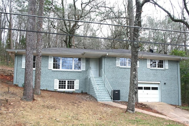 single story home featuring driveway, stairway, an attached garage, brick siding, and central AC unit