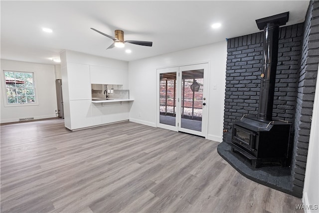 living room with sink, ceiling fan, a wood stove, and light hardwood / wood-style flooring