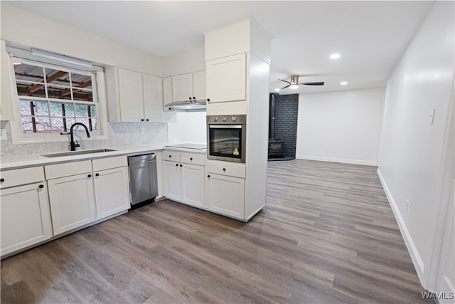 kitchen featuring stainless steel appliances, white cabinets, sink, and a wood stove