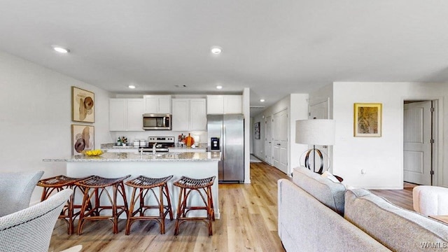 kitchen with a breakfast bar, light stone countertops, appliances with stainless steel finishes, light hardwood / wood-style floors, and white cabinetry