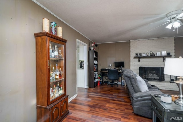 living room featuring a brick fireplace, ornamental molding, a textured ceiling, ceiling fan, and dark wood-type flooring