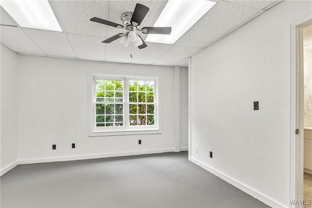 empty room with ceiling fan, a drop ceiling, and concrete floors