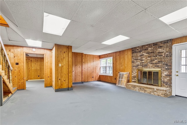 basement featuring a paneled ceiling, a brick fireplace, and wooden walls