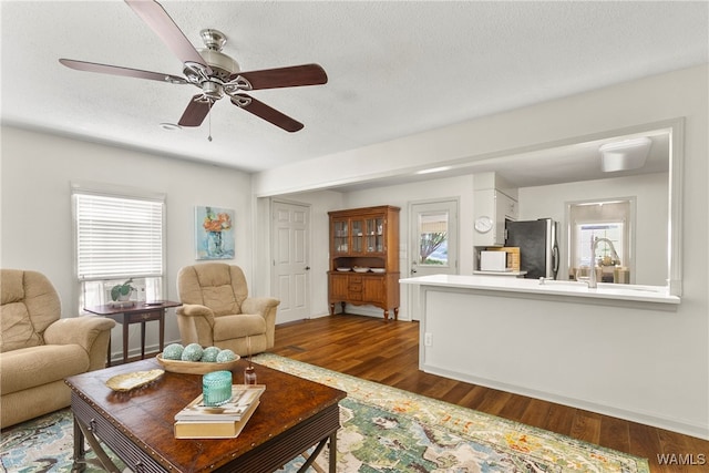 living room with a textured ceiling, ceiling fan, sink, and dark wood-type flooring