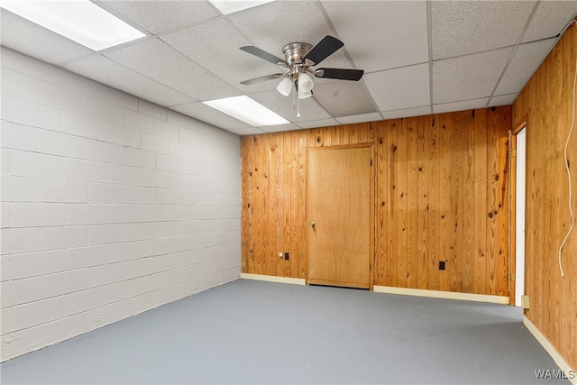 spare room with a paneled ceiling, concrete floors, ceiling fan, and wooden walls