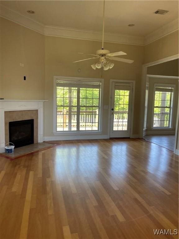 unfurnished living room with crown molding, ceiling fan, a fireplace, wood finished floors, and visible vents