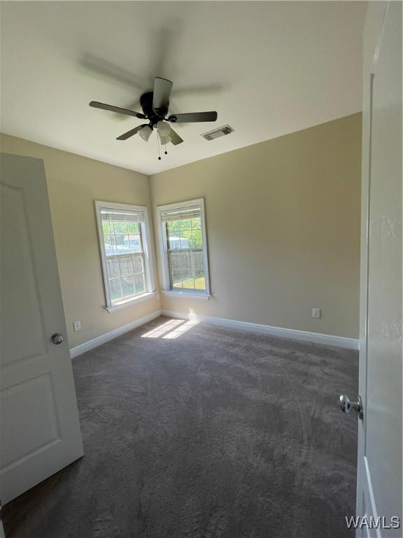 empty room featuring baseboards, a ceiling fan, dark carpet, and visible vents