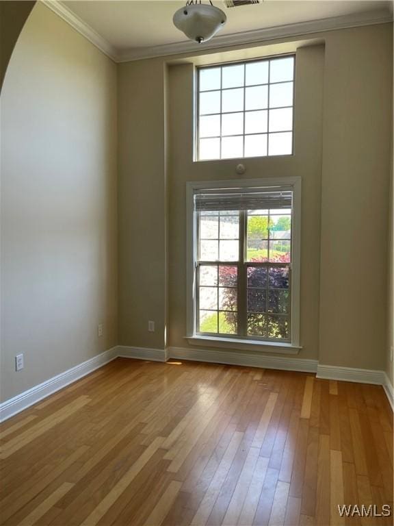 unfurnished room featuring plenty of natural light, ornamental molding, baseboards, and hardwood / wood-style flooring