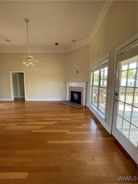 unfurnished living room with ceiling fan, crown molding, light wood-type flooring, a tile fireplace, and baseboards