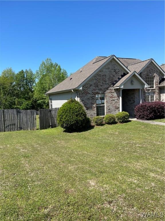 view of side of home with a lawn, brick siding, and fence