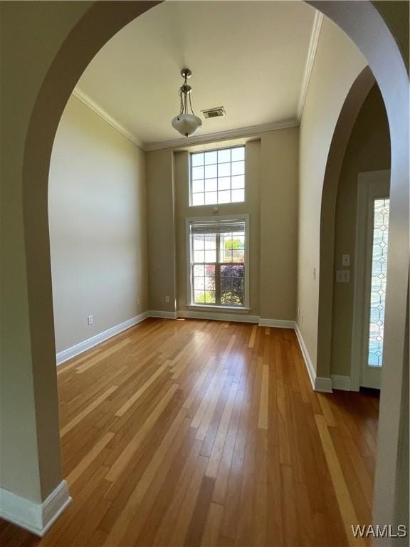 empty room featuring visible vents, crown molding, hardwood / wood-style floors, baseboards, and arched walkways